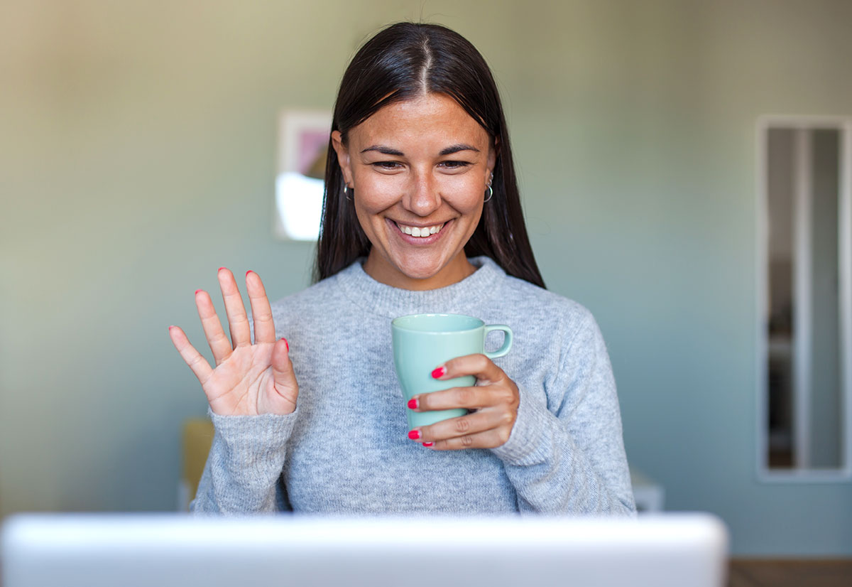 A woman waving at a laptop screen